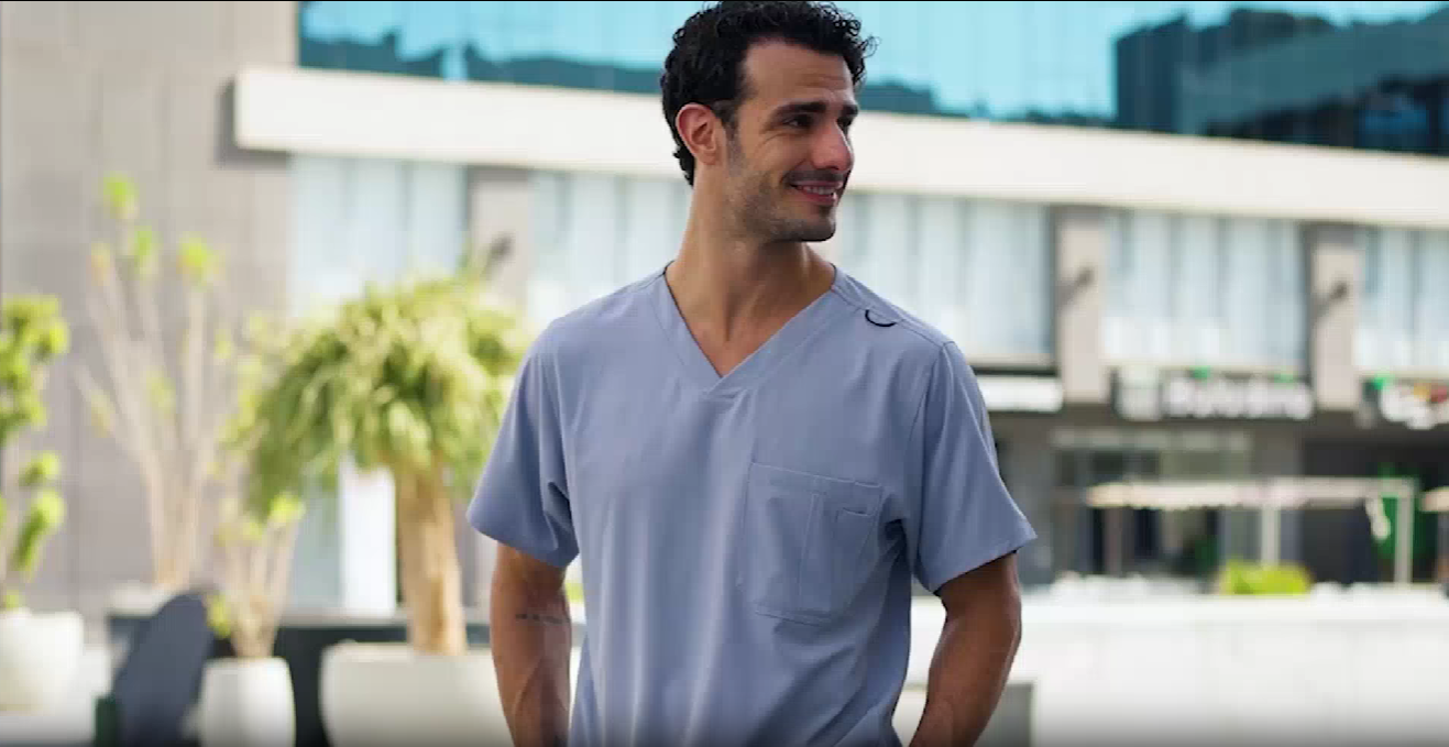 Man wearing a light blue Nike t-shirt standing outdoors with buildings and plants in the background